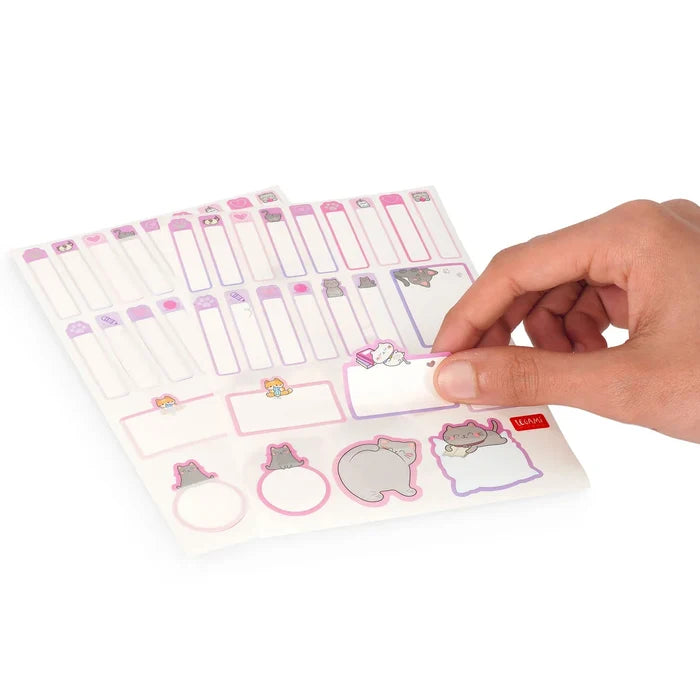Sheet of name tag stickers with cute cat-designs, held by a hand on a white background