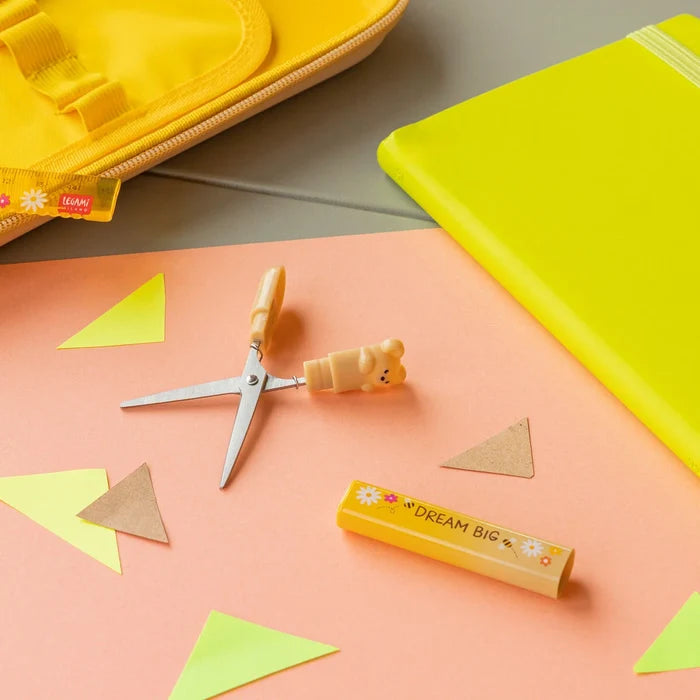 Stationery items including scissors, a rubber, and geometric shapes on a pink surface with a yellow notebook.