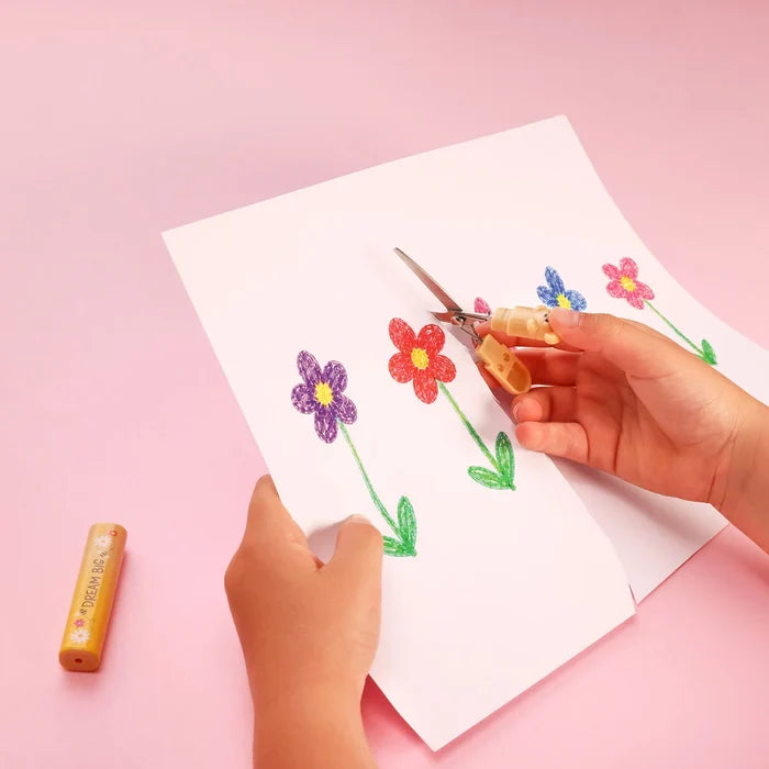 Kid hand cutting out colorful flower drawings from paper with scissors on a pink background