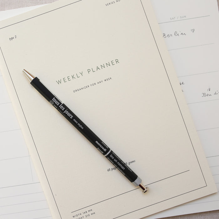 A black ballpoint pen with a 0.5 mm tip on top of a weekly planner notebook.