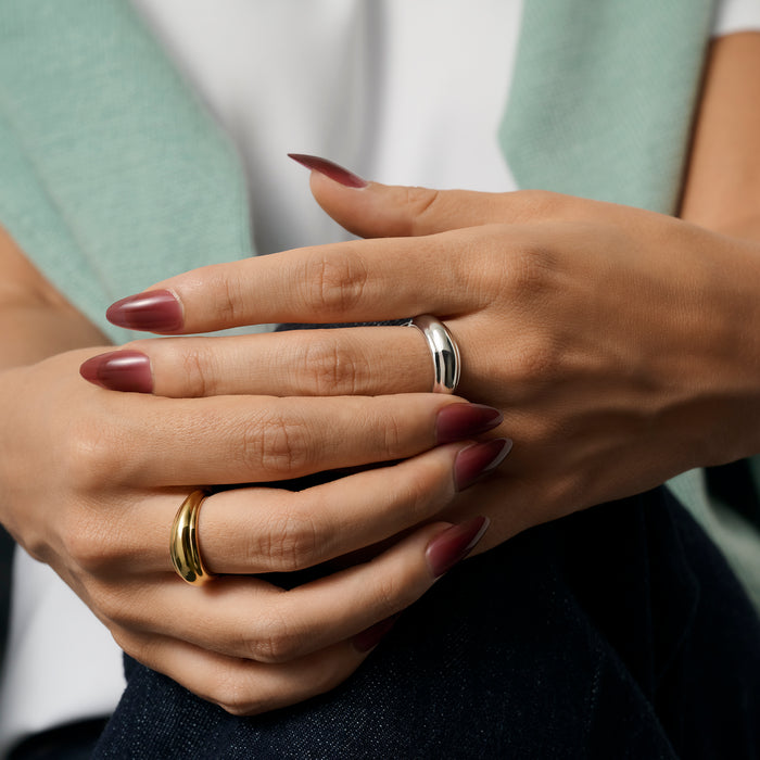 Close-up of a person's hands with dark burgundy manicured nails, wearing two curved dome rings in gold and silver, against a soft mint green and white top. Nickel-free, waterproof & tarnish-resistant stainless steel rings.

Gros plan sur les mains d'une personne aux ongles manucurés bourgogne foncé, portant deux bagues dôme galbées, l'une dorée et l'autre argentée, sur un haut vert menthe et blanc. Bagues en acier inoxydable sans nickel.