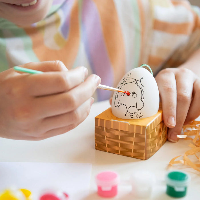 Person decorating an Easter egg with a small brush and paint on a wooden block.