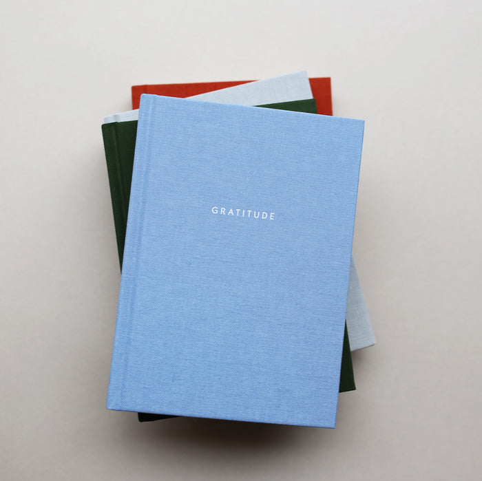 Light blue hardcover Gratitude journal on a stack of books.