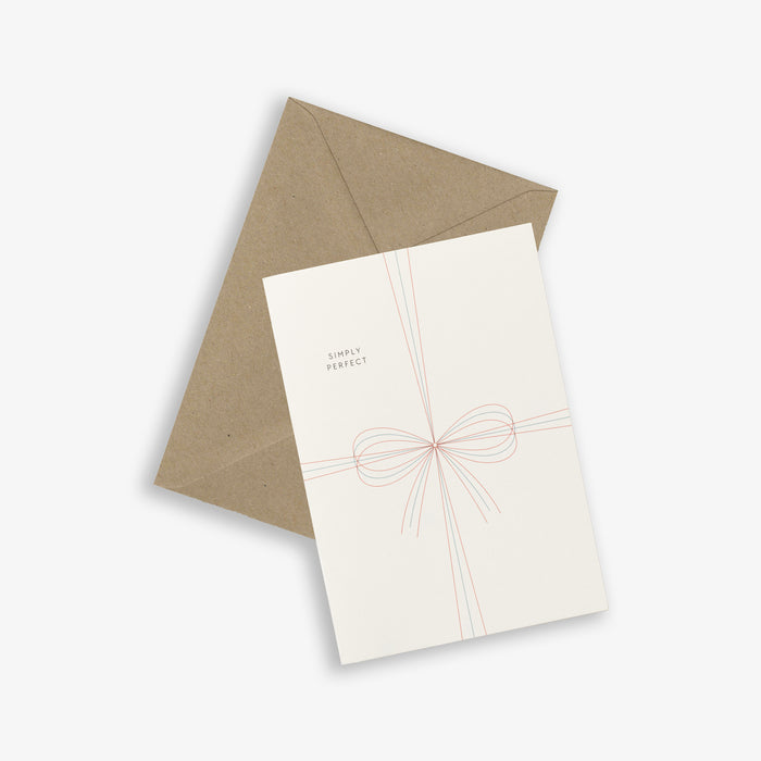 A simple white A6 greeting card with the text 'SIMPLY PERFECT' and a graphic of a bow, accompanied by a brown kraft envelope.