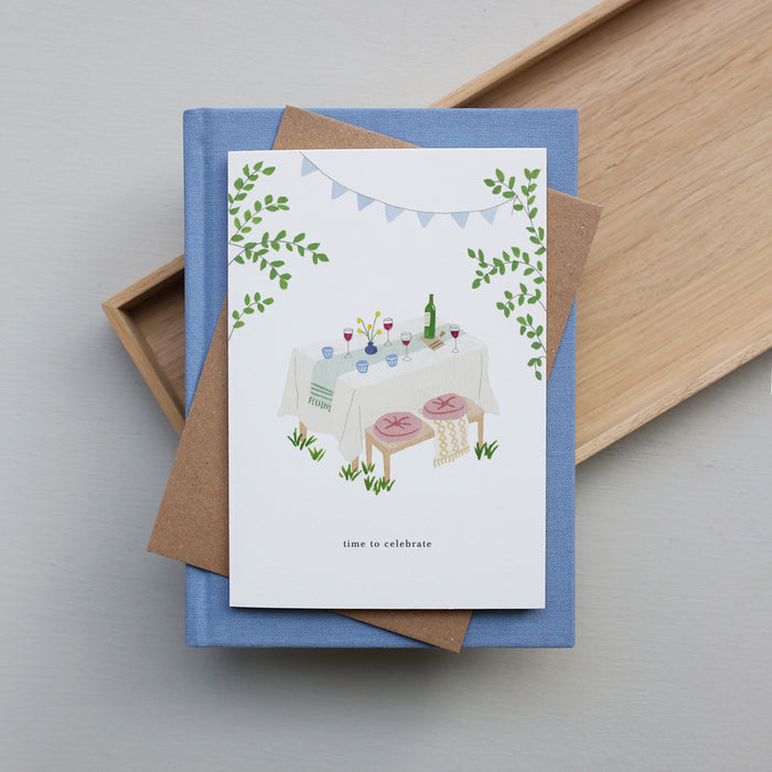 Greeting card with a festive table illustration with the text 'time to celebrate' on a blue book with a brown interior.