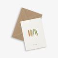A greeting card with a colorful stick illustration and the phrase 'live in color' accompanied by a brown kraft envelope, both placed on a white background.