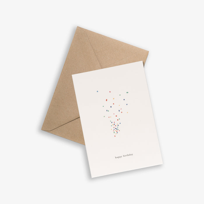 A birthday greeting card with confetti design and the text 'happy birthday' on it, accompanied by a brown kraft envelope.