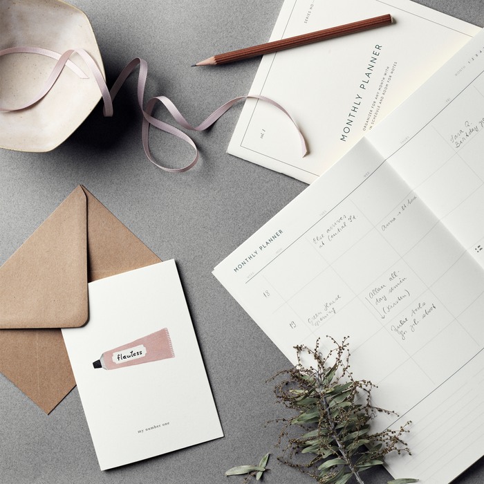 A simple, illustrated greeting card with a 'flawless' cream and the text 'my number one' on it, accompanied by a brown kraft envelope. And a Monthly Planner notebook.