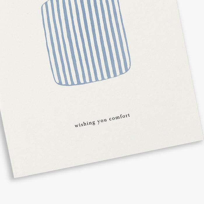 A greeting card with a illustration of a blue and white striped duvet with a sleeping bear and the text 'wishing you comfort', placed on a white background.