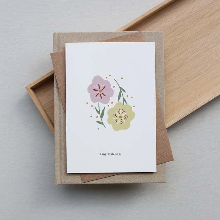 Greeting card with floral design and 'congratulations' text, placed on a wooden tray.