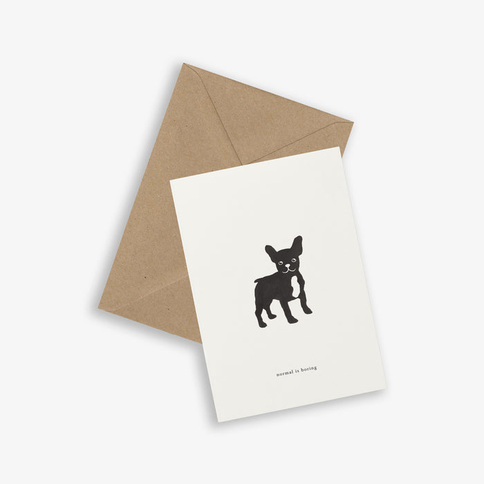 A greeting card with a silhouette of a frenchie on it with the text 'normal is boring', accompanied by a brown kraft envelope.