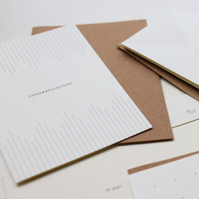 A simple, illustrated greeting card with the text 'Congratulations' printed in the center, accompanied by a brown kraft envelope. The card features a striped pattern in shades of red and blue.