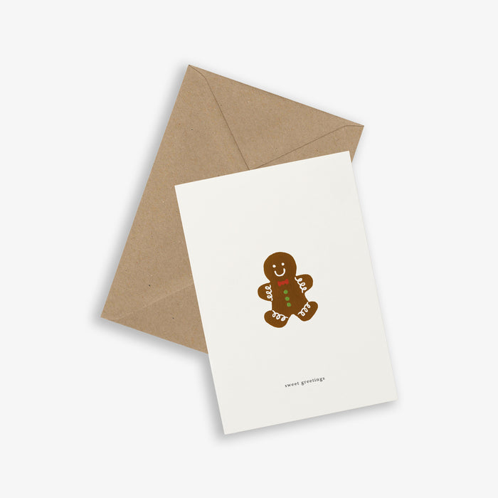 A simple illustrated greeting card with a gingerbread person design, accompanied by a brown kraft envelope. The card is folded and displays the text 'sweet greetings'.