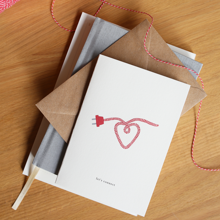 Greeting card with a red cord shaped as a heart with the text 'let's connect' on top of a stack of books.