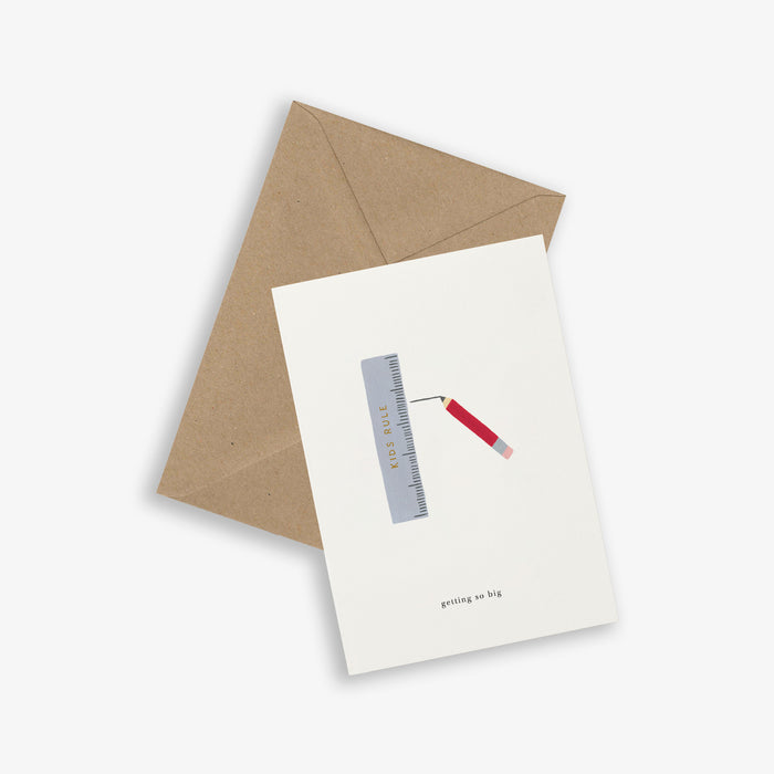 A greeting card with an illustration of a ruler and a pencil and with the text 'getting so big', accompanied by a brown kraft envelope, on a white background.