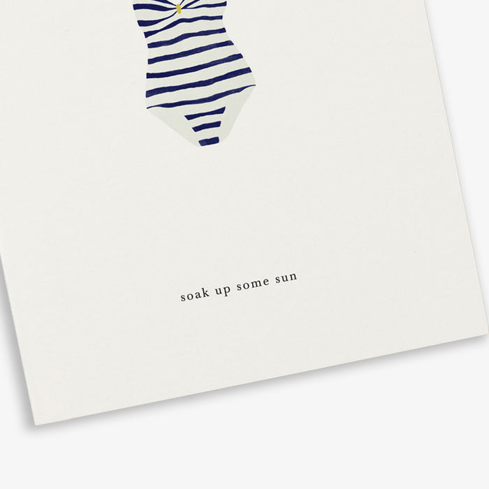 A greeting card with a striped swimsuit illustration and the text 'soak up some sun'.