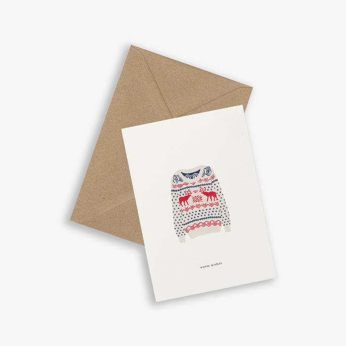 A Christmas-themed greeting card with a sweater pattern and the text 'warm wishes' on it, accompanied by a brown kraft envelope.