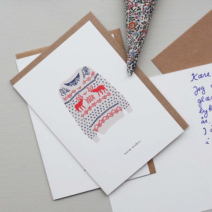 A Christmas-themed greeting card with a sweater pattern and the text 'warm wishes' on it, accompanied by a brown kraft envelope.