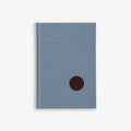 A light blue hardcover notebook with a simple design and a dark brown circular detail on the cover.