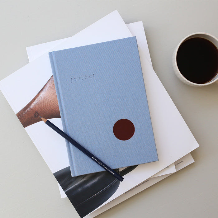 Table setup with a light blue hardcover notebook and a pencil.