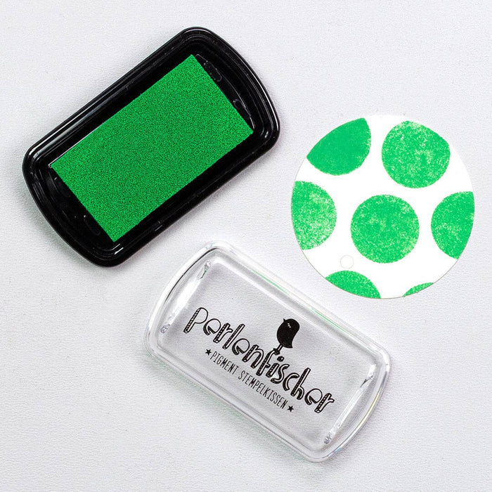 Green ink pad, clear stamp with green polka dots, and black ink pad on a white background