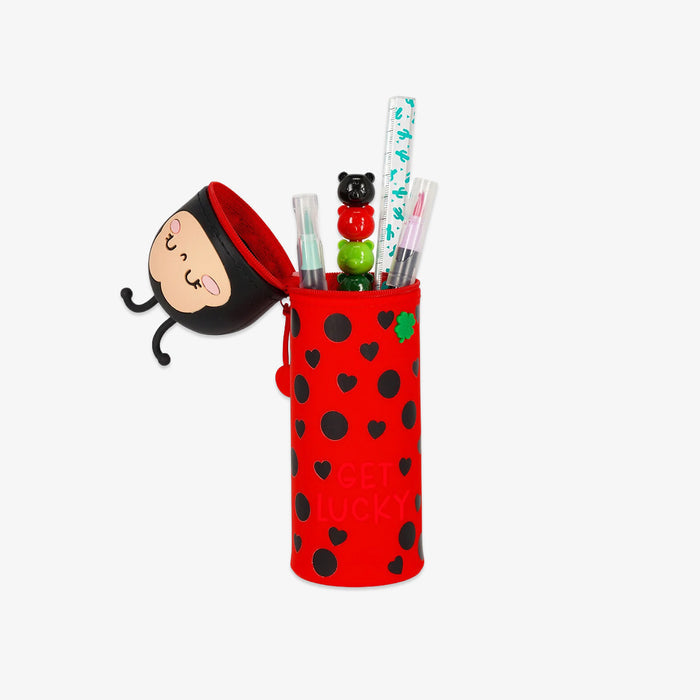 Red pencil case with black polka dots and a cartoon face, containing pens and a small figurine