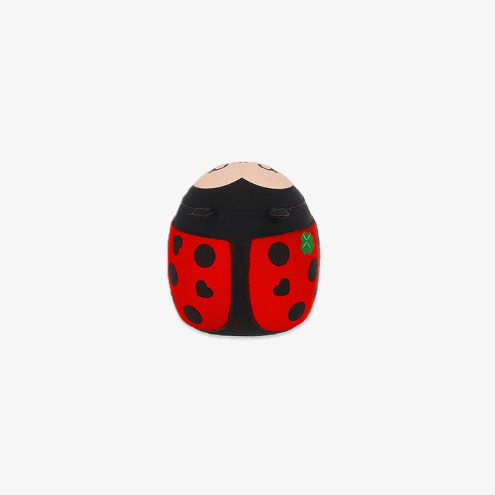A small ladybug-shaped pencil sharpener centered on a plain light gray background. The item has a black top with a beige curved line and two small dark oval details, and red lower sections with black spots and a small green accent.