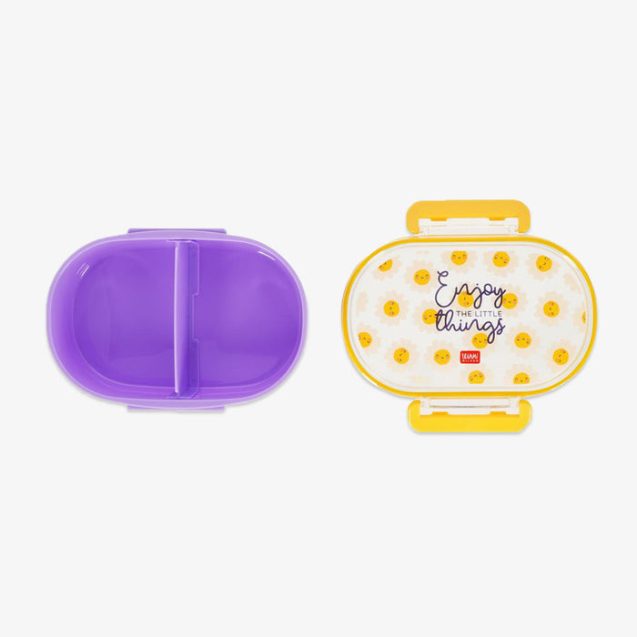 Open plastic lunch box on a light gray background. Purple divided and a transparent lid with yellow dots, the word 'Enjoy the little things' with yellow handles.