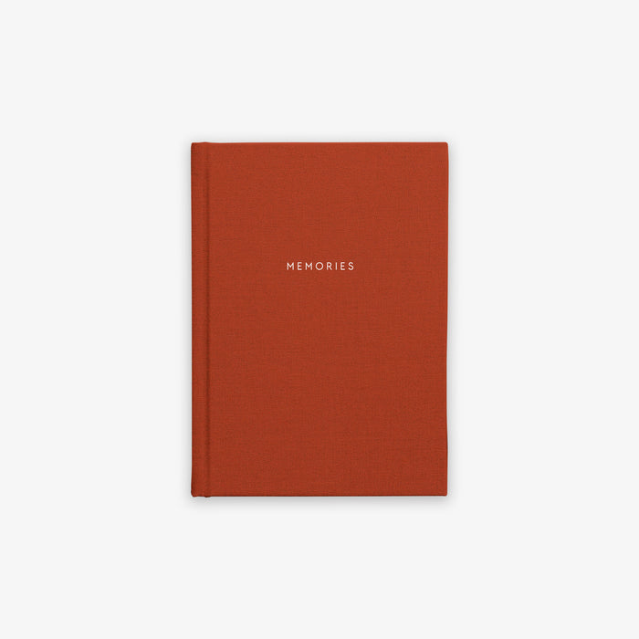 A terracotta-red hardcover notebook with the word 'MEMORIES' embossed on the cover.