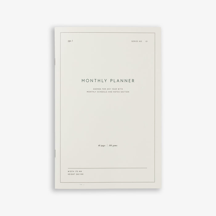 A white monthly planner notebook with text on the cover indicating 'MONTHLY PLANNER NOTEBOOK'.