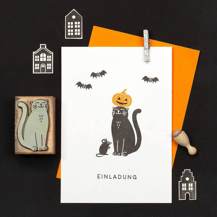 Halloween-themed card with a cat, pumpkin, and bats on a black background.