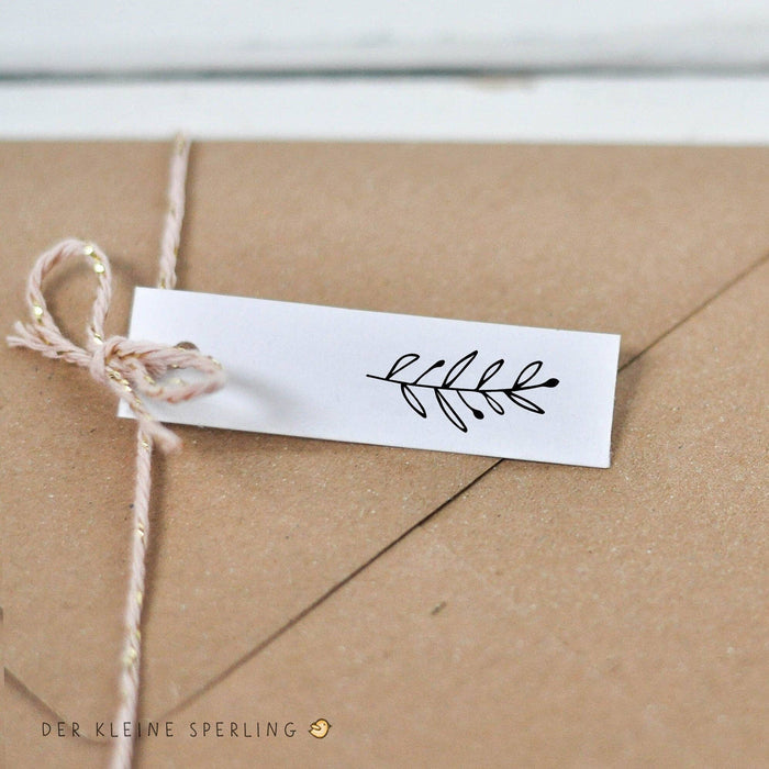 Kraft paper envelope with a white label and decorative plant leaf stamp on a light wooden surface.
