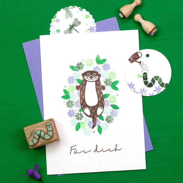 Card with an otter illustration otter and worm surrounded by flowers on a green background