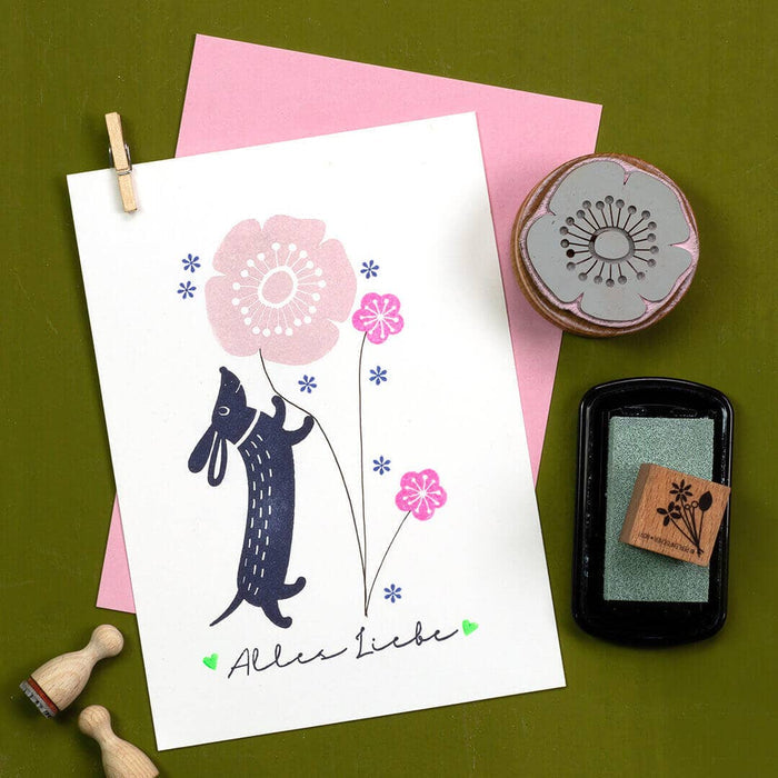 Card with a dog illustration holding flowers, stamps, and ink pad on a green background