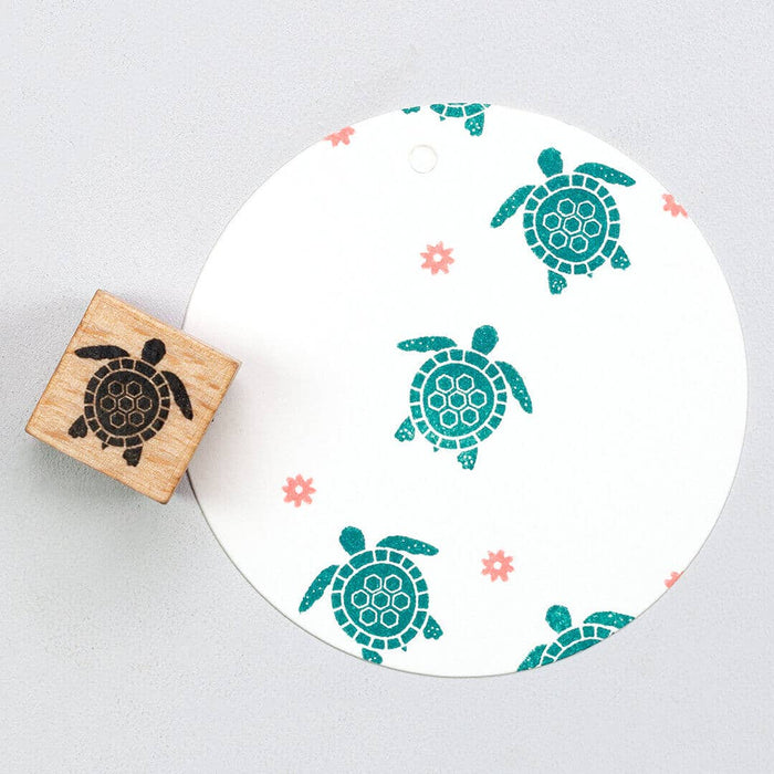 Wooden rubber stamp with turtle design next to a white circular object with turtle patterns on a light gray background