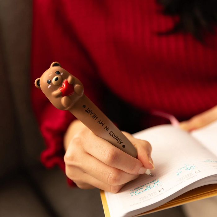 Person holding a pen with a bear design, writing in a notebook.