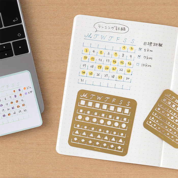 Notebook with calendar stencils on a wooden surface next to a laptop.