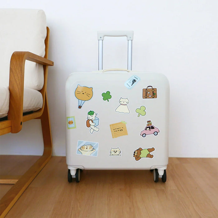 Beige suitcase with cat stickers on a wooden floor next to a chair.
