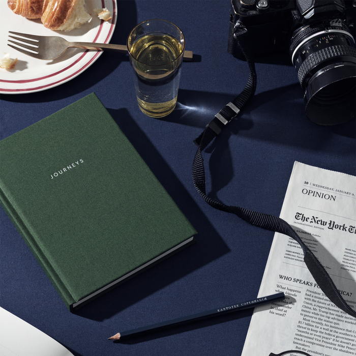 Table setup with a green, hardcover cloth-bound notebook with the word 'JOURNEYS' printed on the cover in capital letters.
