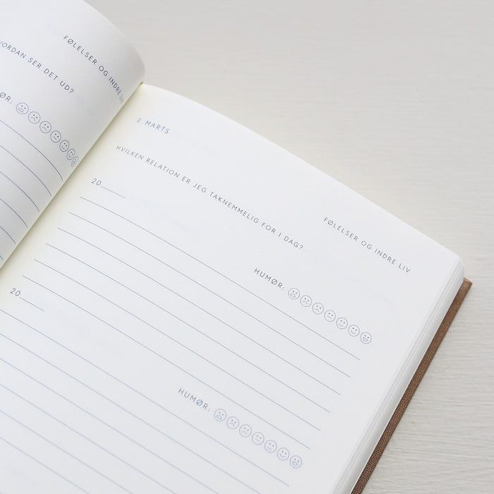 Open notebook with a page showing text and emoji icons from 'Treårsdagbogen' on a light background