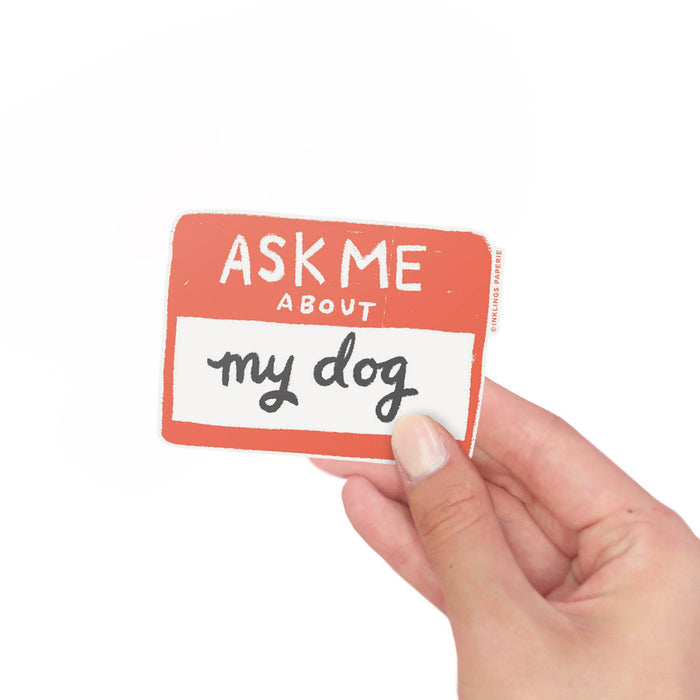 Hand holding a vinyl sticker with 'Ask Me About My Dog' text on a white background