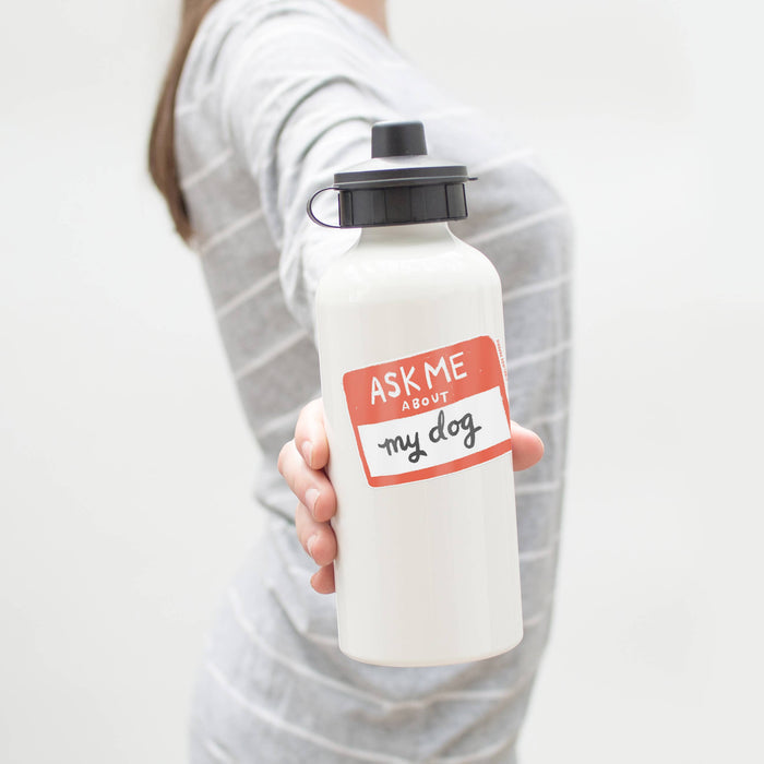 Person holding a white water bottle with a vinyl sticker 'Ask Me About My Dog' on a plain background