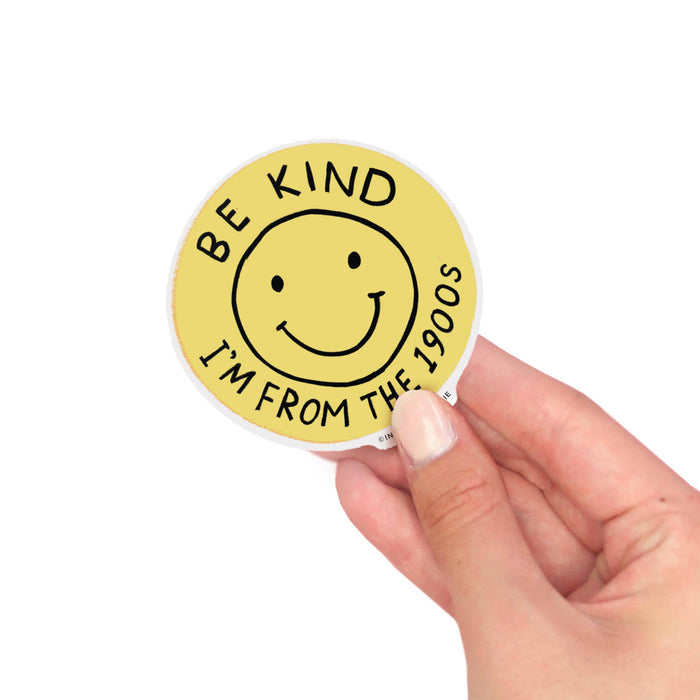 Hand holding a yellow sticker with a smiley face and text on a white background