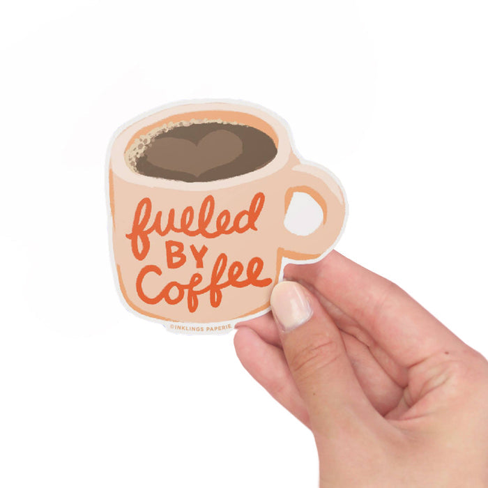 Vinyl sticker of a coffee cup with 'fueled by coffee' text held by a hand on a white background