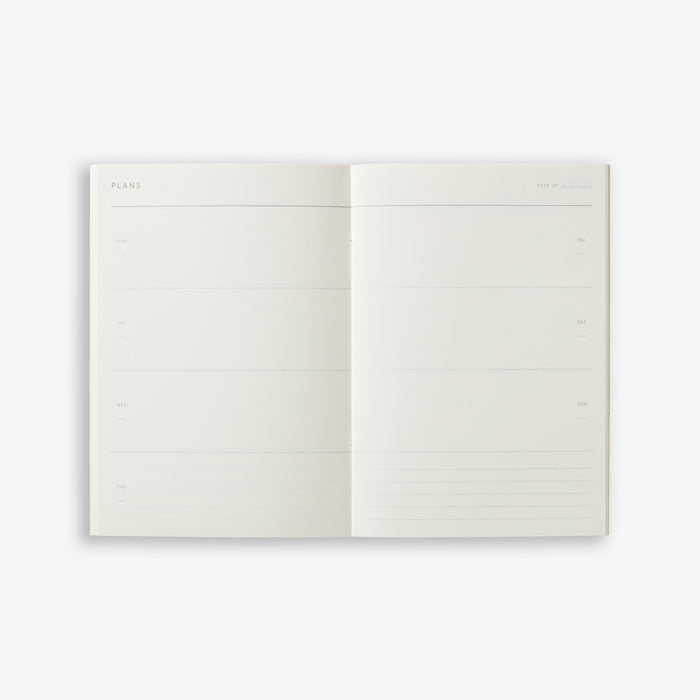 A white weekly planner notebook open on two pages with a weekly overview.