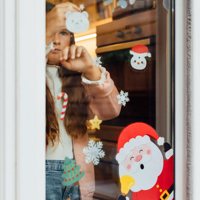 Child decorating a window with Christmas stickers, including Santa Claus and snowflakes.
