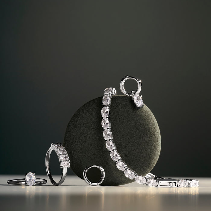 Silver rings, earrings and a tennis bracelet set with oval clear stones, displayed against a round dark stone on a dark background. Nickel-free, waterproof & tarnish-resistant stainless steel jewelry for sensitive skin.

Bagues, boucles d'oreilles anneaux et bracelet tennis argentés sertis de pierres transparentes ovales, présentés contre une pierre ronde foncée sur fond sombre. Bijoux en acier inoxydable sans nickel, résistants à l'eau et anti-ternissement pour peaux sensibles.